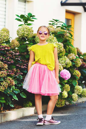 Outdoor portrait of cute little girl wearing green shirt, pink tutu skirt and sunglassesの写真素材
