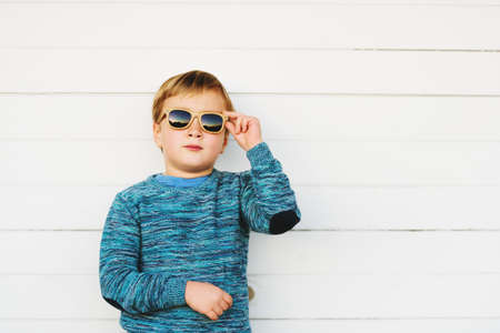 Fashion portrait of adorable toddler boy wearing blue knitted pullover and sunglassesの写真素材