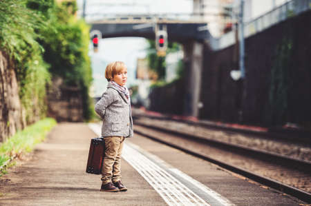 Adorable little boy on a railway station, waiting for the train with suitcaseの写真素材