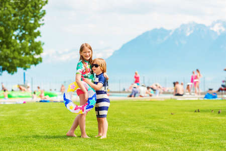 Two adorable kids hugging each other standing by the pool on a hot summer day, wearing swim suitsの写真素材