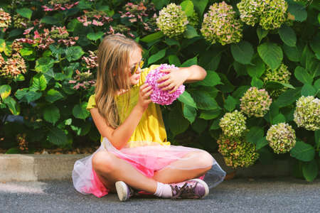 Outdoor portrait of cute little girl wearing green shirt, pink tutu skirt and sunglasses, playing with hydrangea flowersの写真素材