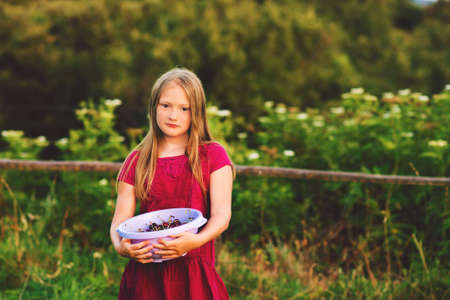 Outdoor portrait of little girl holding a bowl with fresh cherriesの写真素材