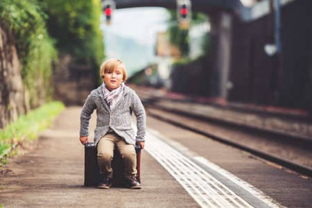 Adorable little boy on a railway station, waiting for the train with suitcaseの写真素材