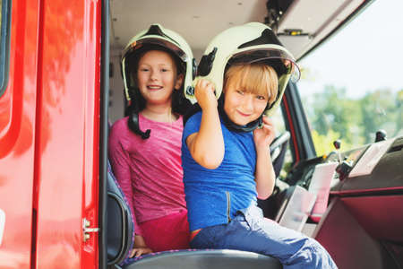 Two cute kids playing in fire truck, pretending to be firefighters, open doors day at fire station....