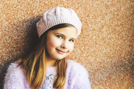 Close up portrait of cute 9 year old little girl with blue eyes, wearing pink hat, standing against brown backgroundの写真素材