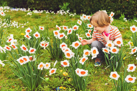 Adorable little blond boy playing with colorful easter eggs in the park, egg hunt