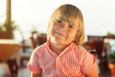 Close up portrait of cute 4 year old little boy on summer vacation, resting on a terrace at sunsetの写真素材