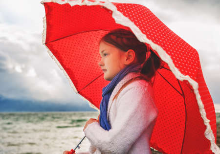 Little girl with big red umbrella next to lake on a very cold dayの写真素材