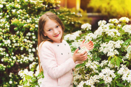 Outdoor portrait of 7-8 year old pretty little girl with spring flowers, wearing pink jacketの写真素材
