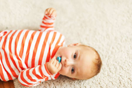 Cute 12-18 month baby boy laying on carpet floor, chewing rubber toyの写真素材