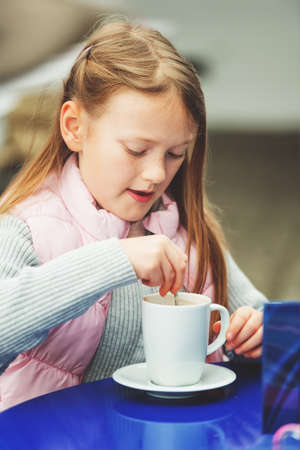 Outdoor portrait of a cute little girl drinking hot chocolate in a cafeの写真素材