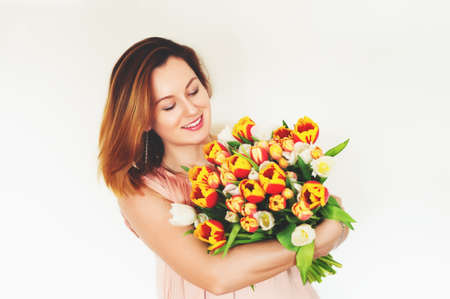 Happy young red hair woman holding big bouquet of red yellow tulips standing against white backgroundの写真素材