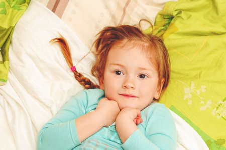 Adorable 3 year old girl lying on a bed, top viewの写真素材