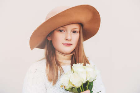 Pretty little girl wearing a hat, holding bouquet of white roses, standing against beige backgroundの写真素材
