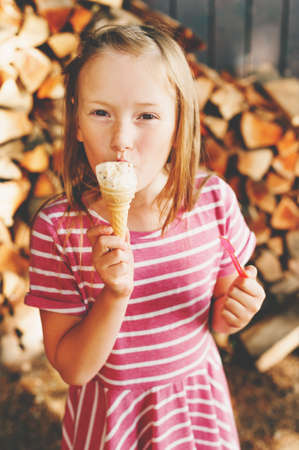 Cute little 6 year old girl eating ice cream outdoors, wearing pink stripe dress, summer pleasures for kidsの写真素材