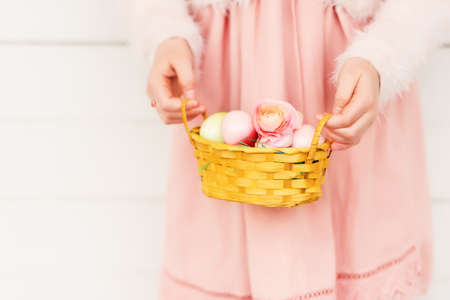 Kid girl holding basket with easter eggs and buttercup flowersの写真素材