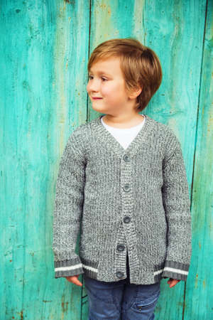 5-6 year old kid boy posing outdoors, wearing grey knitted cardigan, standing against turquoise backgroundの写真素材
