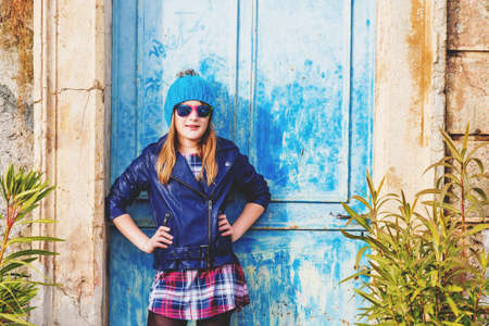 Outdoor fashion portrait of preteen 10-11 years old girl wearing blue leather jacket, hat and sunglassesの写真素材