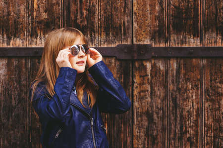 Outdoor fashion portrait of funny 9-10 year old girl wearing sunglasses and blue leather jacketの写真素材