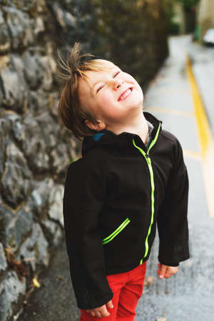 Little 5-6 year old boy playing outdoors in early spring, walking next to road, wearing black...