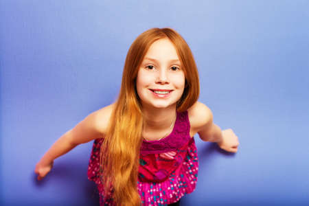 Studio shot of young preteen 9-10 year old redhead girl wearing pink top, standing against blue purple backgroundの写真素材
