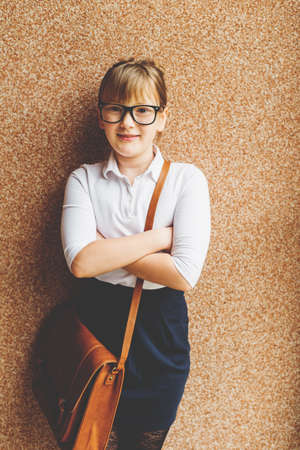 Pretty little 9 year old girl walking back to school, wearing white shirt, black skirt, eyeglasses and brown leather bagの写真素材