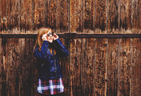 Outdoor fashion portrait of funny 9-10 year old girl wearing sunglasses and blue leather jacket