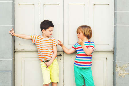 Group of two funny little boys playing together outdoors, wearing colorful tshirts and shorts, summer fashion for kids.の写真素材