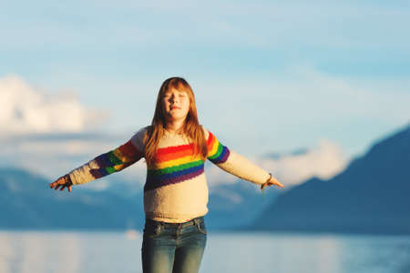 Happy and young kid girl playing next to lake geneva at sunset, arms wide open