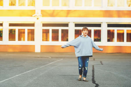 Cute 9 year old kid girl playing on school yard, wearing denim jeans and grey sweatshirtの写真素材