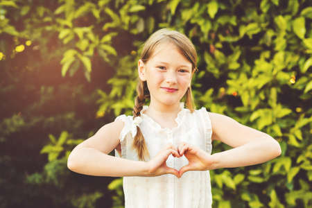 Little girl making heart sign with her hands in the summer garden at sunsetの写真素材