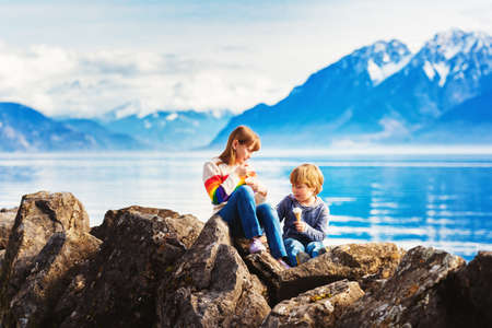 Group of two kids, big sister and little brother, eating ice cream by lake Geneva, Lausanne, Switzerlandの写真素材