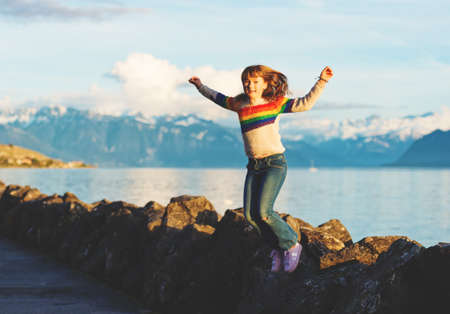 Happy and young kid girl playing next to lake geneva at sunset, arms wide openの写真素材