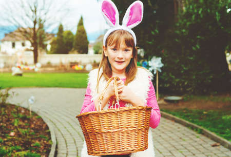 Kid girl with bunny ears and big basket going to egg hunt in spring parc
