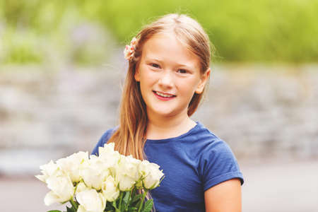 Outdoor portrait of a yong little girl of 9 years old, wearing blue tee shirt, holding fresh bouquet of beautiful white rosesの写真素材
