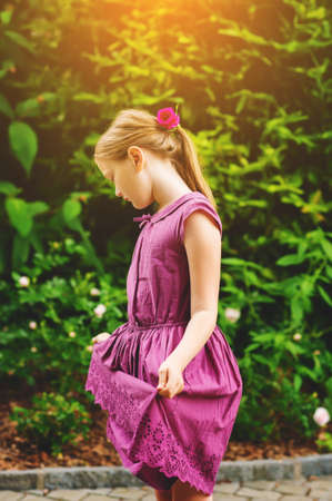 Kid girl playing in the park on a nice and sunny summer day, wearing purple dressの写真素材