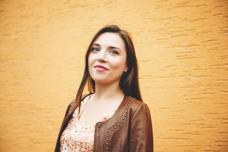Outdoor portrait of young woman with long dark hair, wearing brown leather jacketの写真素材