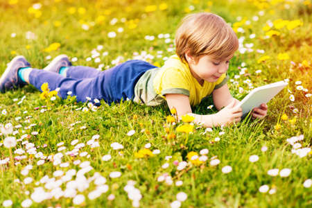 Happy little kid boy playing tablet PC outdoors in the park on a very sunny dayの写真素材