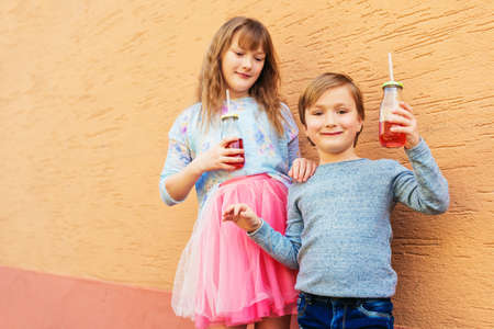 Outdoor portrait of two funny fashion kids, holding drinks, wearing blue and pink clothesの写真素材