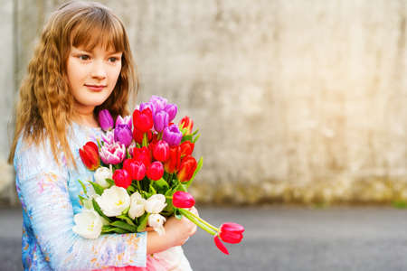 Outdoor portrait of a sweet kid girl with big bouquet of colorful tulipsの写真素材