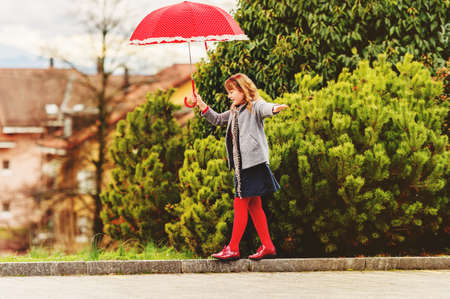 Funny little girl playing outdoors with big red polkadot umbrellaの写真素材