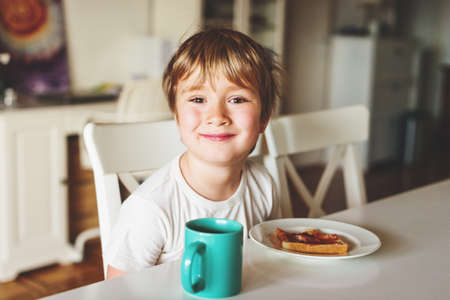 Cute little boy eating his toast with jam and hot chocolate for breakfastの写真素材