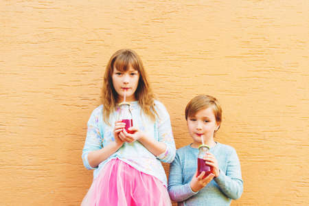 Outdoor portrait of two funny fashion kids, holding drinks, wearing blue and pink clothesの写真素材