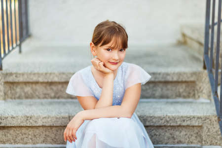 Sweet little preteen girl wearing party dress, sitting on stairsの写真素材
