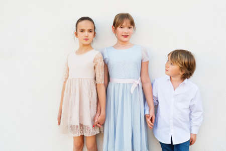 Group of three kids, 2 girls and one boy, wearing party clothes, standing against white backgroundの写真素材