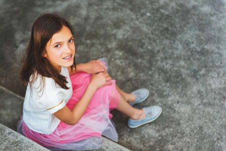 Preteen girl with teeth braces wearing beautiful dress, sitting on stairs, top viewの写真素材