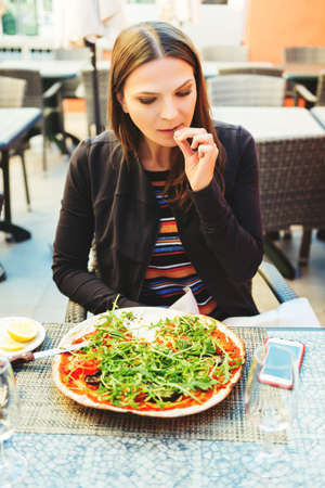 Young fit woman eating vegetarian pizza in the restaurantの写真素材