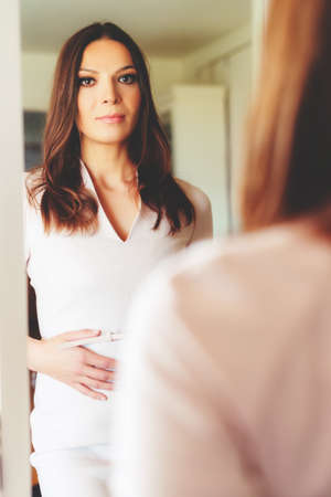 Portrait of beautiful brunette woman looking in the mirror, 30-35 year old