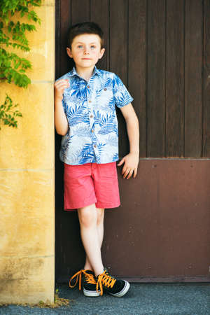 Funny stylish kid boy posing outdoors, wearing blue print shirt and red shortsの写真素材