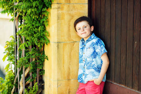 Funny stylish kid boy posing outdoors, wearing blue print shirt and red shortsの写真素材